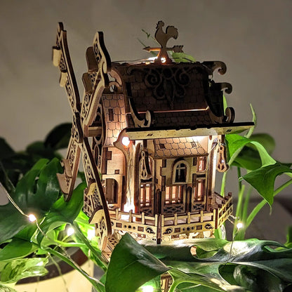 A cozy, moody night shot of a glowing 3D toy windmill hidden inside green houseplant leaves, made from laser cut plywood.