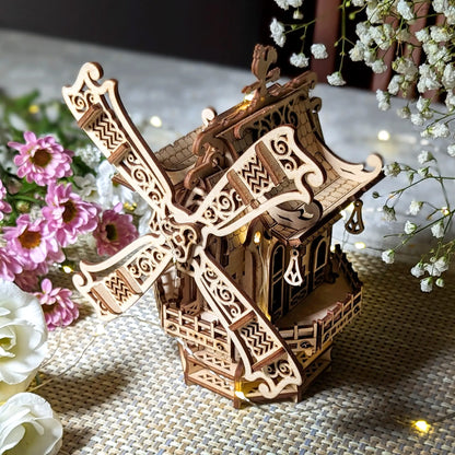 High-angle view of an ornate 3D windmill with warm fairy lights and fresh pink flowers, made of detailed laser cut plywood.