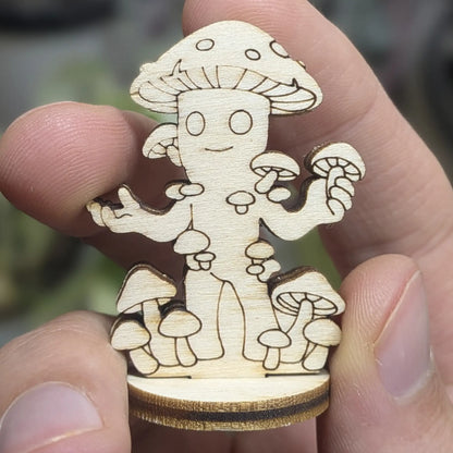 Hand holds a laser cut plywood mushroom folk miniature. Detailed front view shows engraved spots, cute eyes and small arms