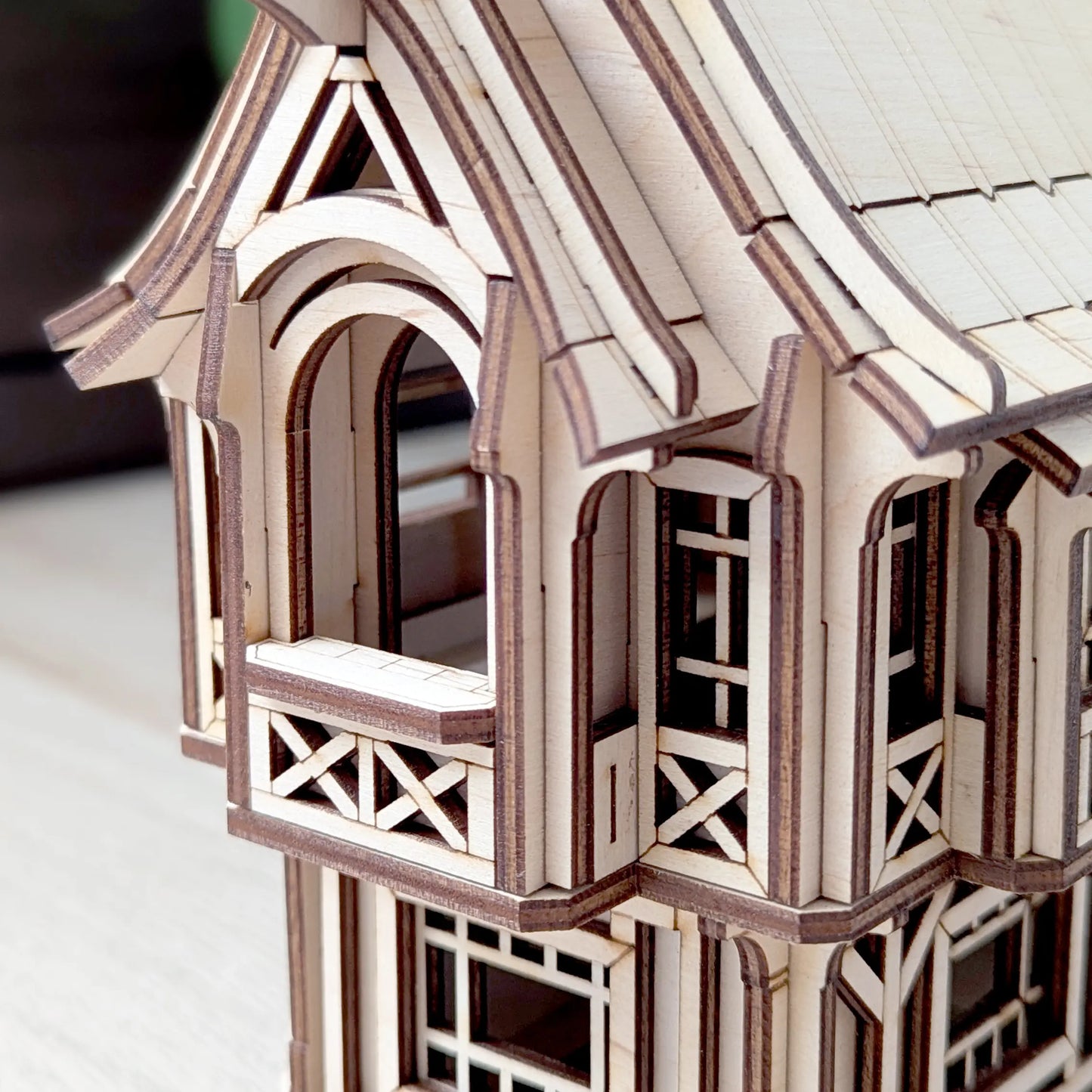 Completed laser cut plywood old village house model styled on a white table with house plants and wooden character figures.