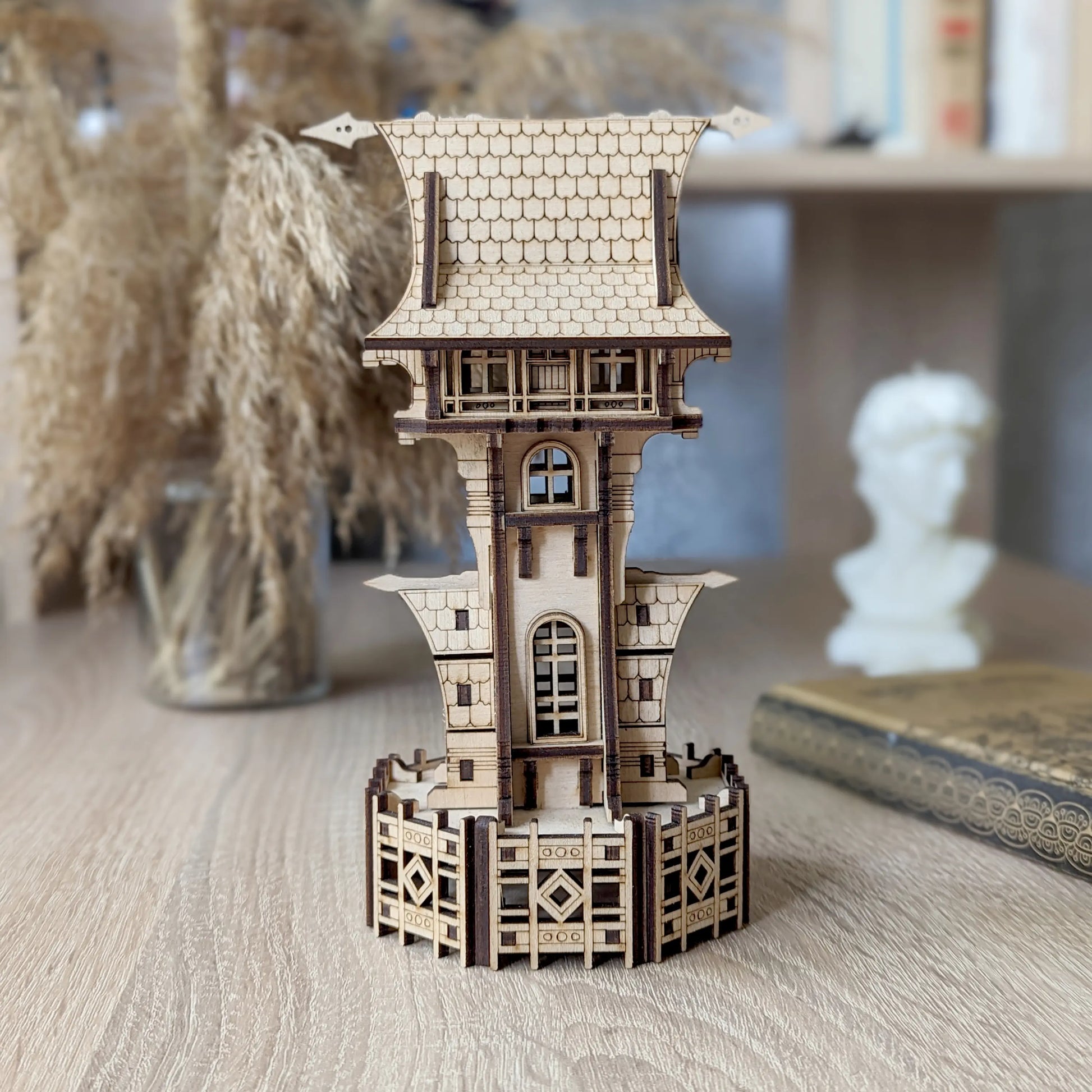 Miniature fairy castle tower made of laser cut plywood stands on a wooden desk next to a white bust decor.