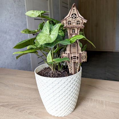 Laser cut plywood garden tower with a ground stake inserted into a white potted plant with green leaves.