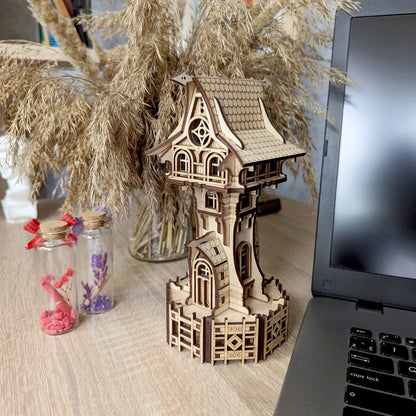 Laser cut plywood miniature tower sits on a table near a laptop, dried grass bouquet, and glass bottles.