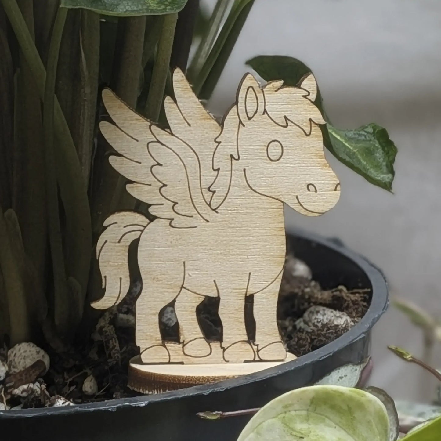 Laser cut plywood Pegasus figurine stands in a plant pot. Features engraved wings, mane, and tail on a natural wood base