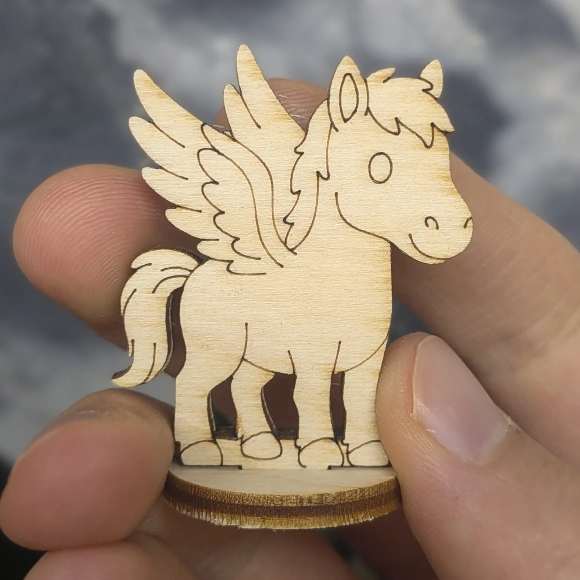 Hand holds a laser cut plywood Pegasus for scale. Detailed engraved feathers and mane shown in natural light wood tones