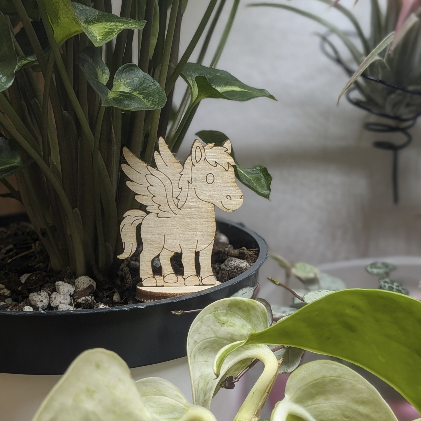 Laser cut plywood Pegasus figurine stands in a plant pot. Features engraved wings, mane, and tail on a natural wood base