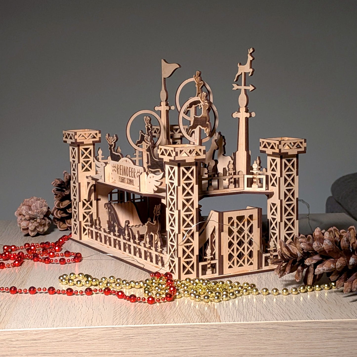 Angled front view of the assembled wooden “Reindeer Flight School” model made from a laser cut digital file, featuring standing reindeer figures and tall tower structures.