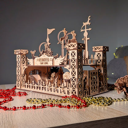 Wooden “Reindeer Flight School” display made from a laser cut digital design, featuring layered reindeer silhouettes on raised posts and a sleigh scene below, styled with pinecones and festive lights