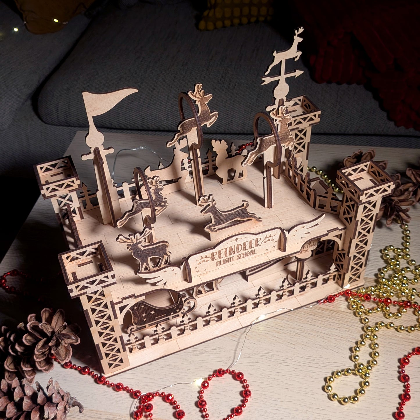 Top angled view of the assembled wooden “Reindeer Flight School” model made from a laser cut digital file, showing multiple reindeer figures, platforms, and sleigh details.