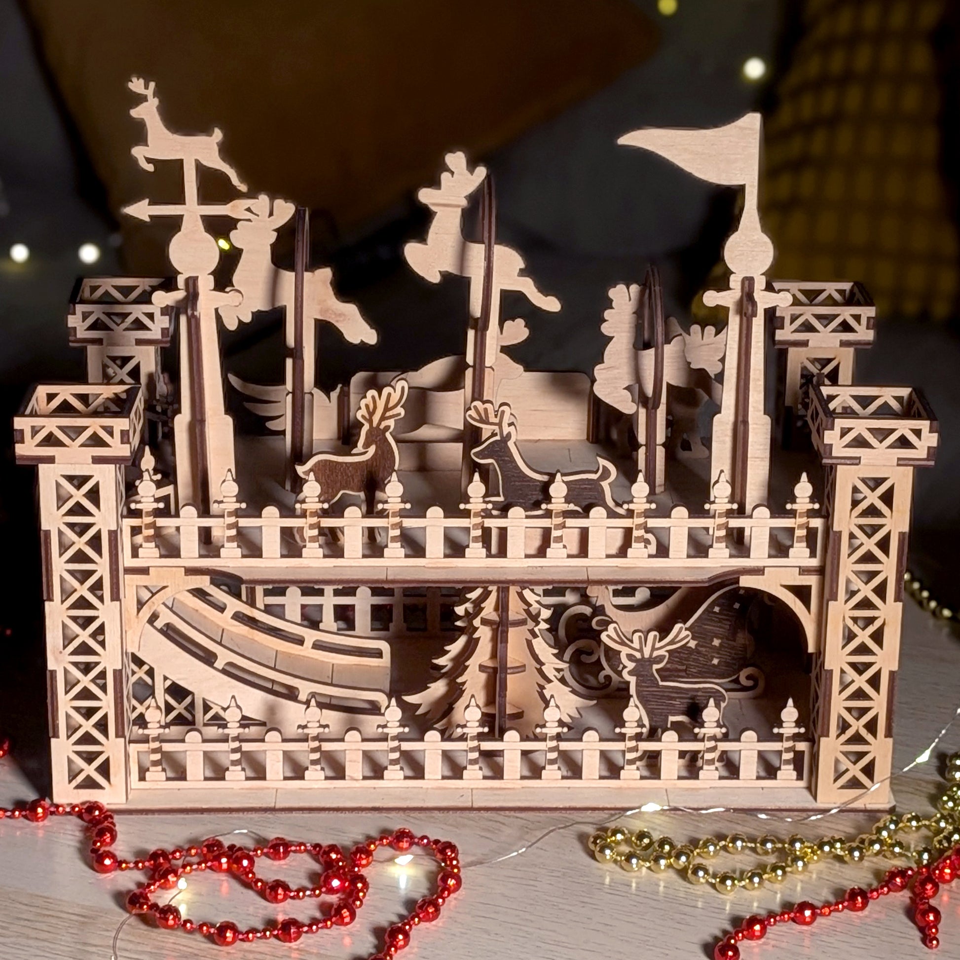 Back view of the assembled wooden “Reindeer Flight School” scene made from a laser cut digital file, with reindeer figures, towers, fences and sleigh, displayed on a table with holiday beads