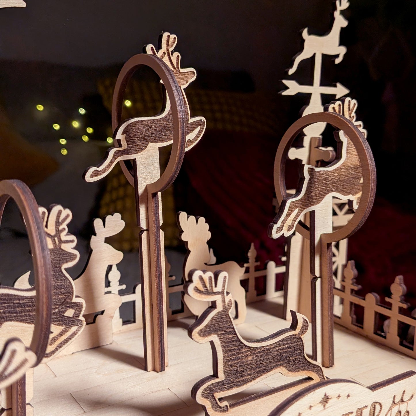Close-up of wooden reindeer figures jumping through circular training hoops in a holiday scene made from a laser cut digital file, showing layered shapes and engraved detailing