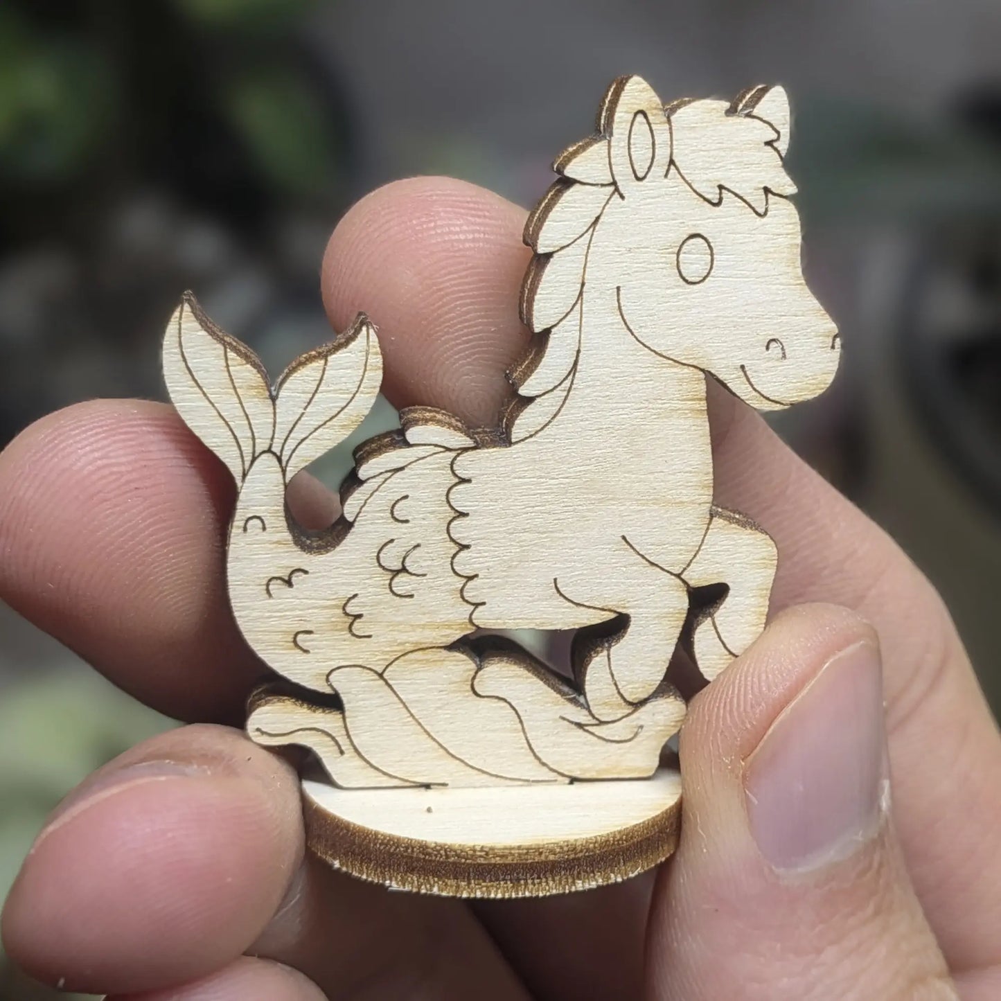 Small laser cut plywood seahorse held in hand. Shows intricate etched scales, horse mane, and dark burnt edges for detail