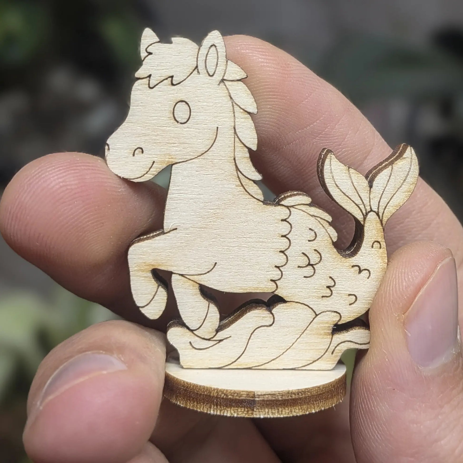 Handheld laser cut plywood mythical seahorse facing right. Detailed engraving shows fish tail, horse head, and wood texture