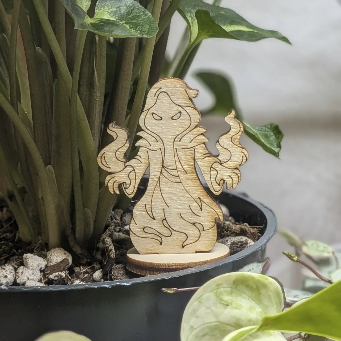Shadow mage figurine of laser cut plywood stands in a plant pot. Features a hooded robe and magic swirls on natural wood