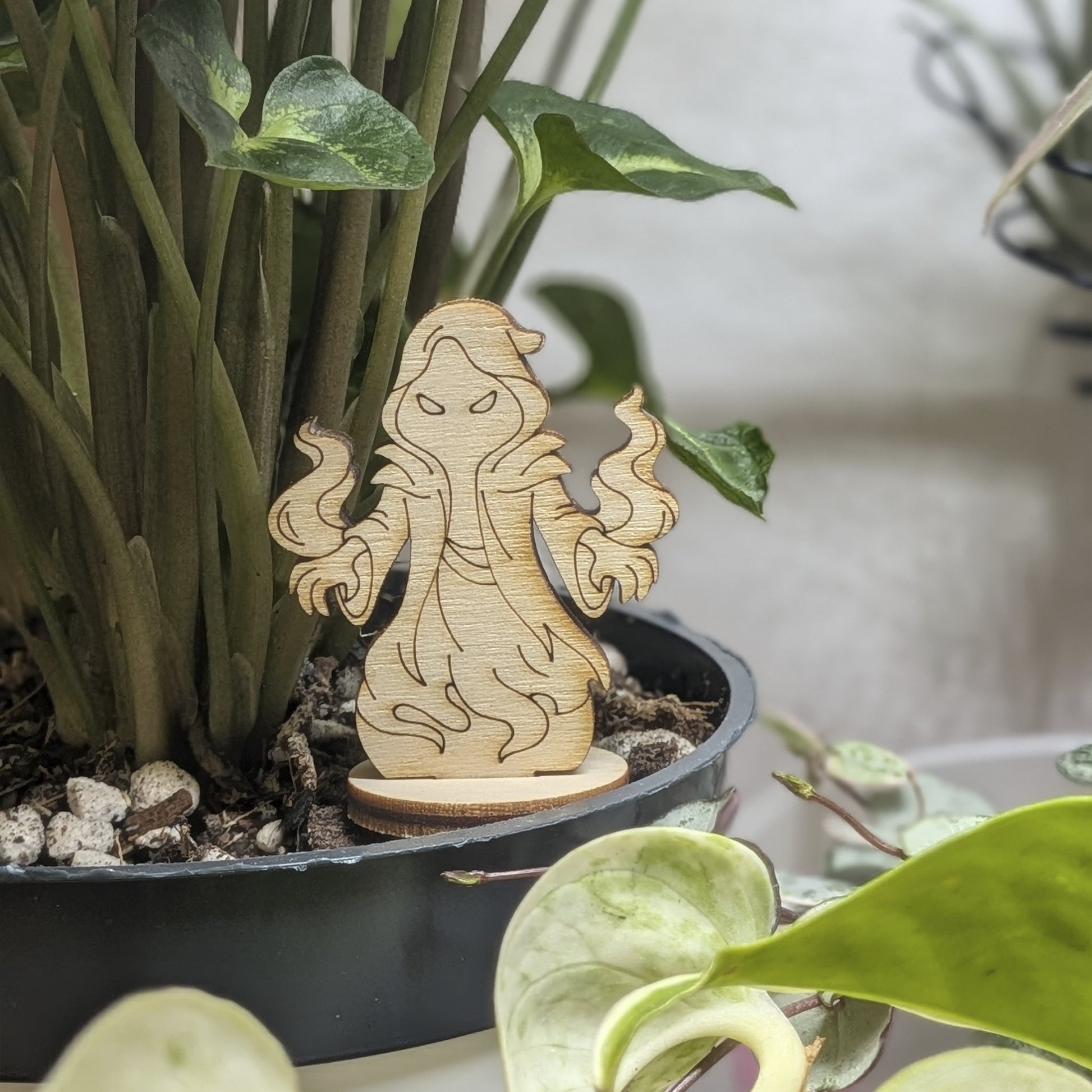 Shadow mage figurine of laser cut plywood stands in a plant pot. Features a hooded robe and magic swirls on natural wood
