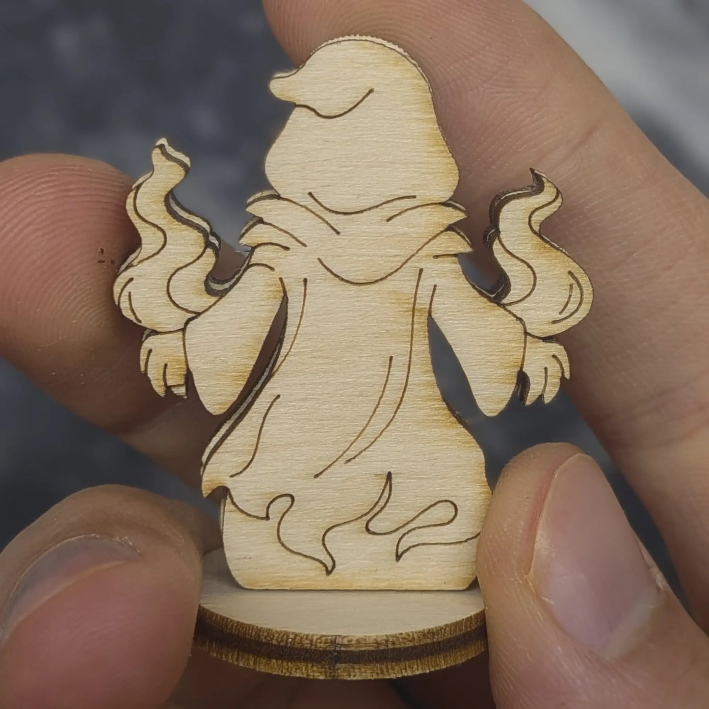 Back view of a laser cut plywood shadow mage held in hand. Highlights the dark burnt edges and smooth wood grain texture