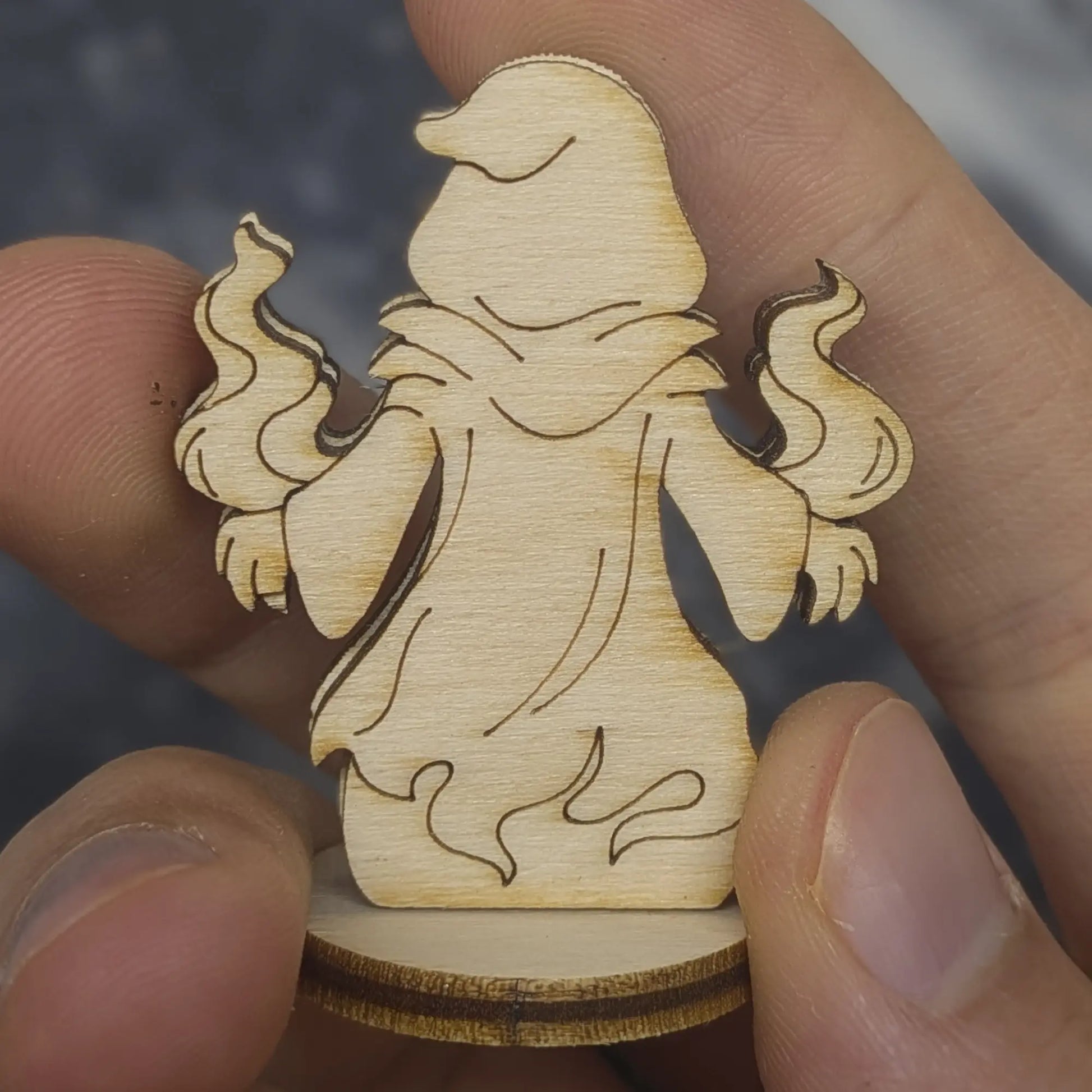 Back view of a laser cut plywood shadow mage held in hand. Highlights the dark burnt edges and smooth wood grain texture
