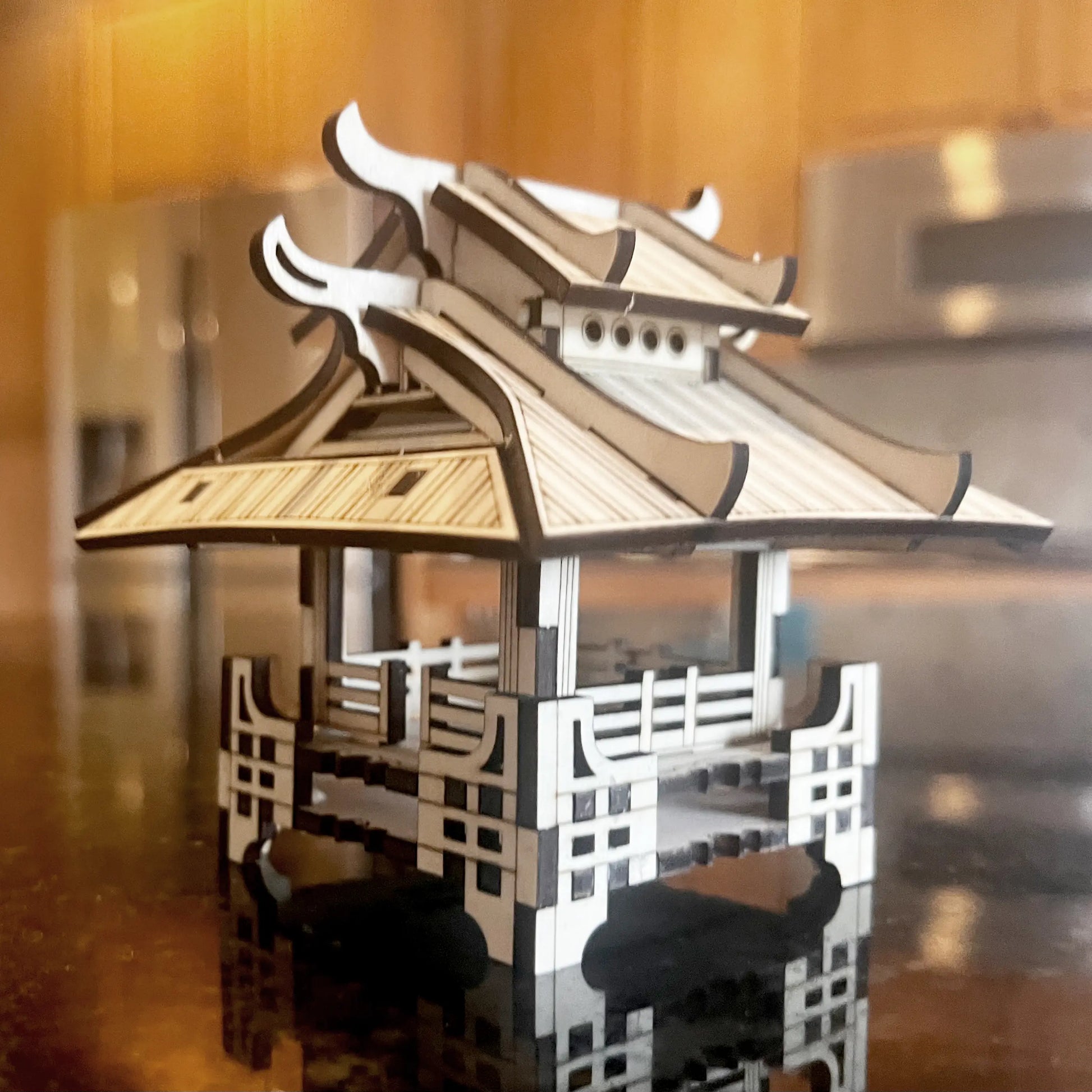 Miniature asian pagoda model made of laser cut plywood, showcasing a double-tiered roof on a glossy dark kitchen counter.