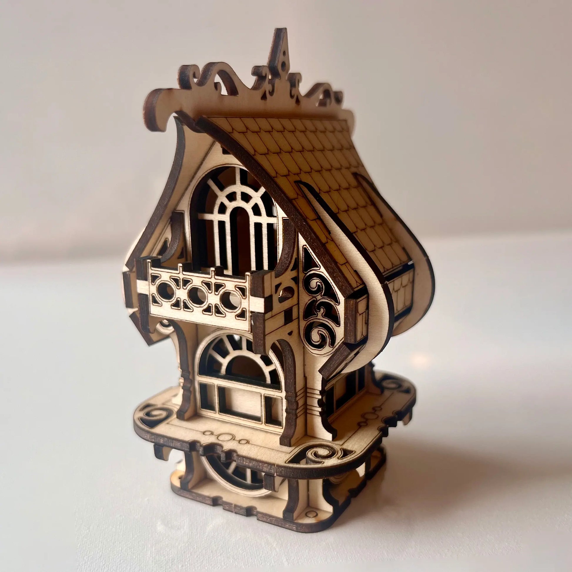 Intricate laser cut plywood elf house featuring decorative filigree, balcony, and ornate roof. Isolated on white background.