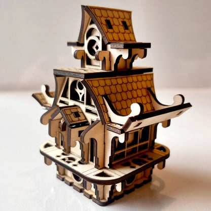 Small decorative fairy house made of laser cut plywood. Intricate roof tiles and gothic windows with precise wood details.