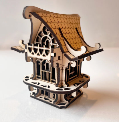 Miniature fairy house made of laser cut plywood. Features intricate roof tiles, decorative balconies, and wood details.