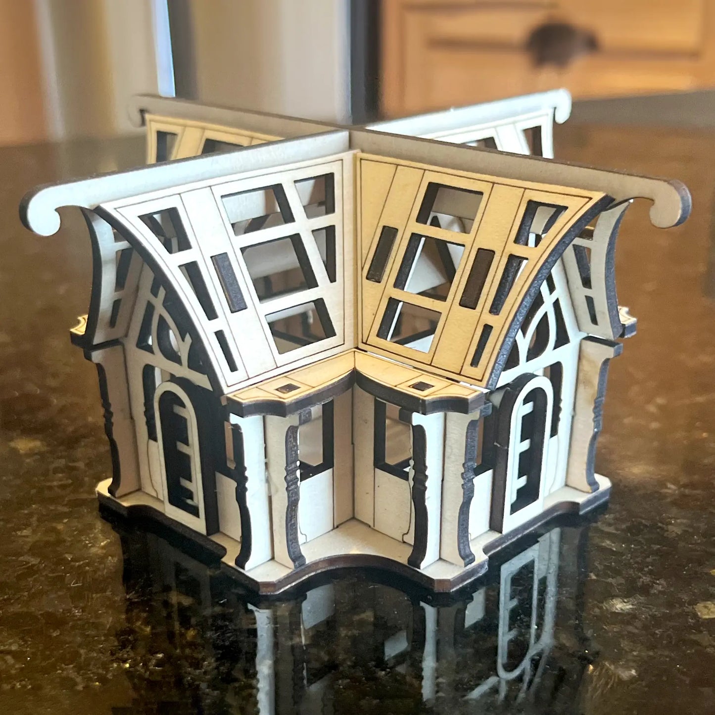 Miniature laser cut plywood greenhouse lantern centerpiece standing on a glossy dark kitchen counter, home staging.