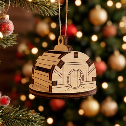 Laser cut plywood miniature barn ornament with a round door, hanging on a Christmas tree with blurry bokeh lights.
