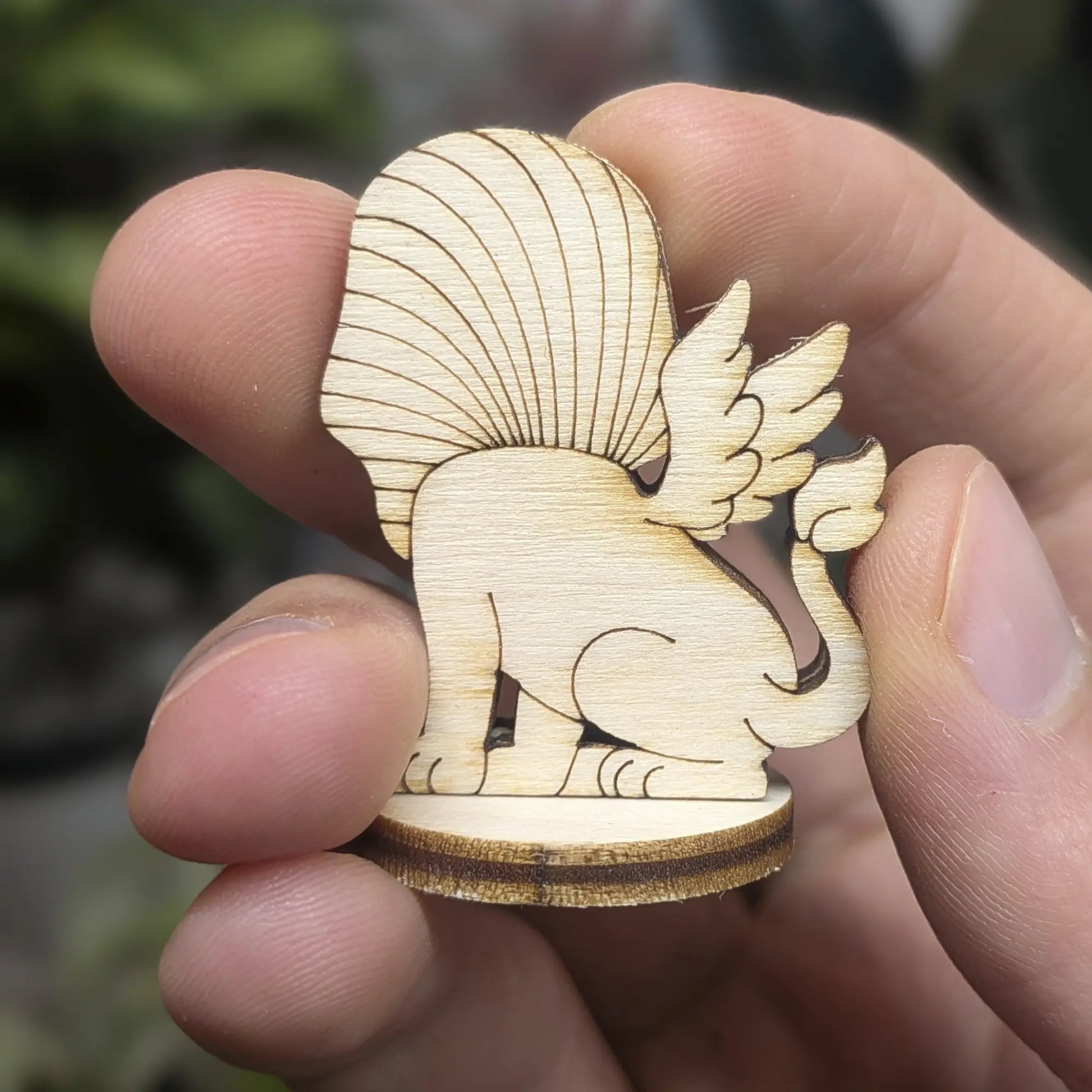 Back view of a laser cut plywood sphinx held in hand. Highlights detailed wing feathers and the large pharaonic headpiece