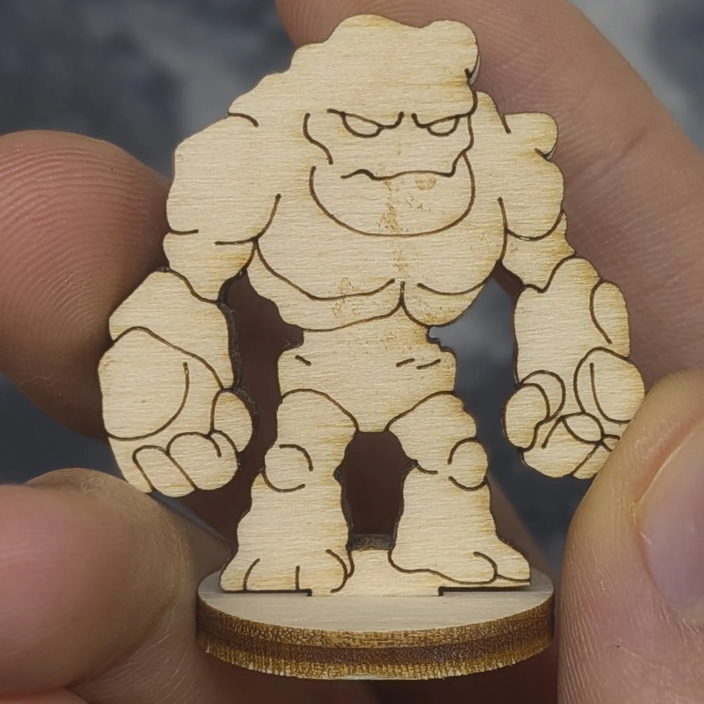 Hand holds a laser cut plywood stone golem for scale. Front view shows jagged rock segments and engraved facial features