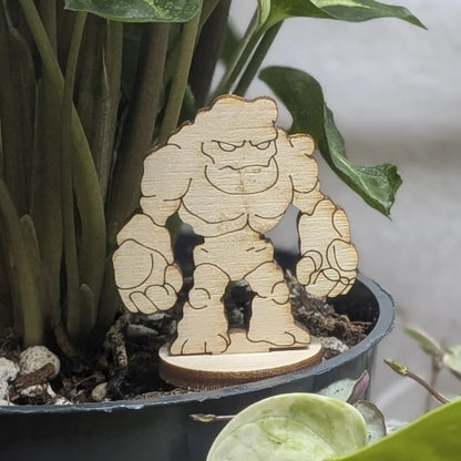 Laser cut plywood stone golem sits in a plant pot. Features jagged rocky body, blank eyes, and natural wood grain texture