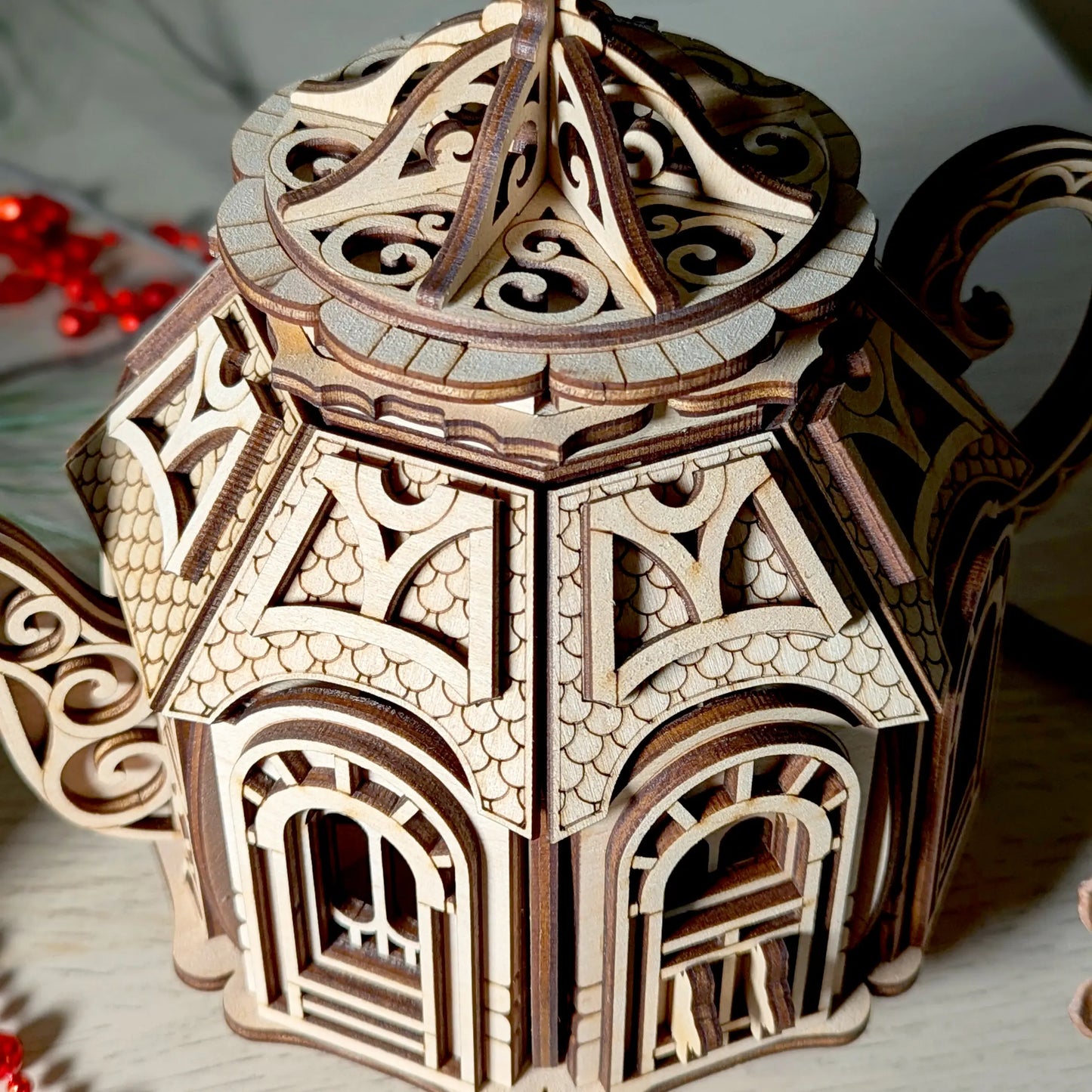 High-angle view of the detailed filigree lid and scale roof patterns on a laser cut plywood teapot figurine.