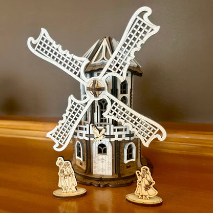 Assembled laser cut plywood windmill model with two detailed character standees shown on a warm wooden tabletop surface.