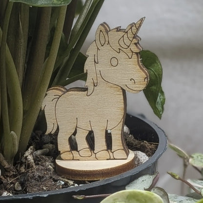 Laser cut plywood unicorn figurine stands in a plant pot. Features engraved spiral horn, mane, and tail on a round base