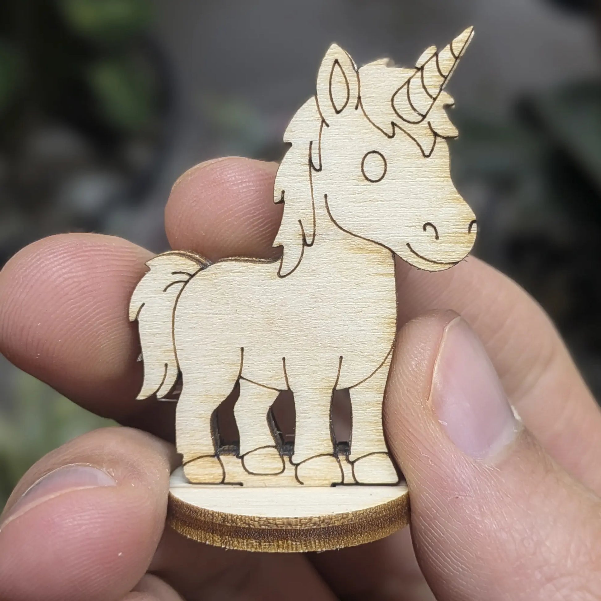 Hand holds a mini unicorn of laser cut plywood. Showing engraved spiral horn and mane details at a small tabletop scale.