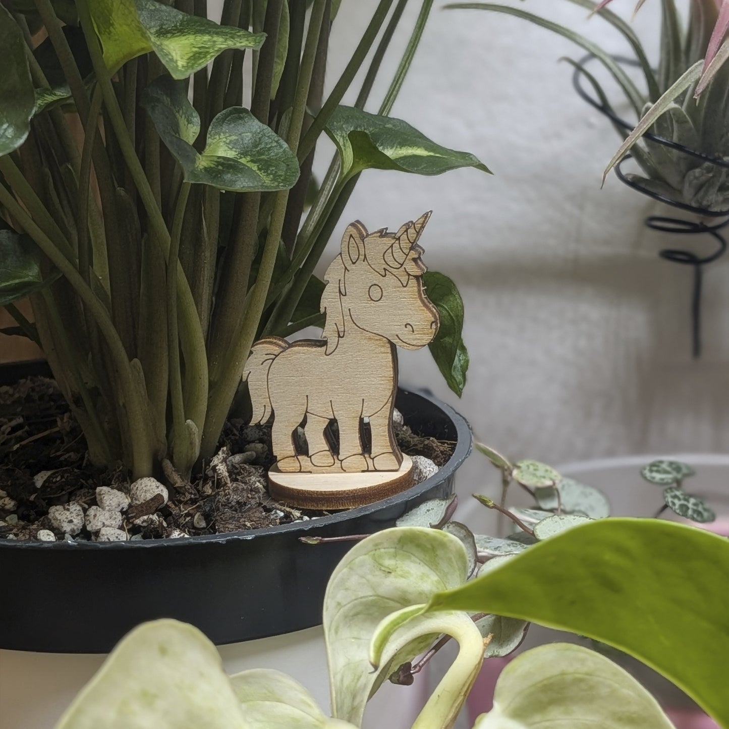 Laser cut plywood unicorn figurine stands in a plant pot. Features engraved spiral horn, mane, and tail on a round base
