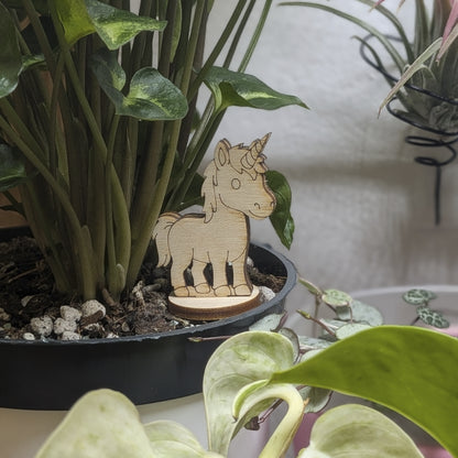 Laser cut plywood unicorn figurine stands in a plant pot. Features engraved spiral horn, mane, and tail on a round base