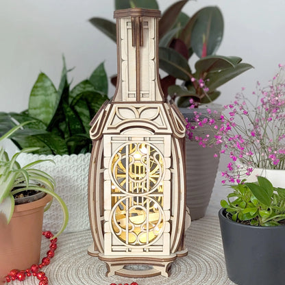Front narrow view of a laser cut plywood jug fairy house illuminated from within by warm fairy lights, next to houseplants.