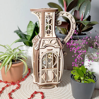 Full view of a whimsically shaped laser cut plywood jug fairy house styled on a table with indoor potted plants and beads.