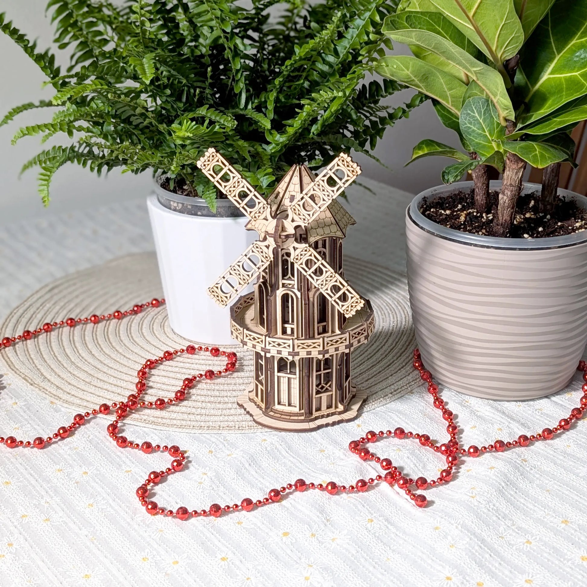 Finished laser cut plywood Victorian windmill model staged on a table between two different vibrant green houseplants.