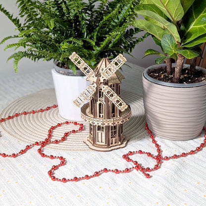 Finished laser cut plywood Victorian windmill model staged on a table between two different vibrant green houseplants.