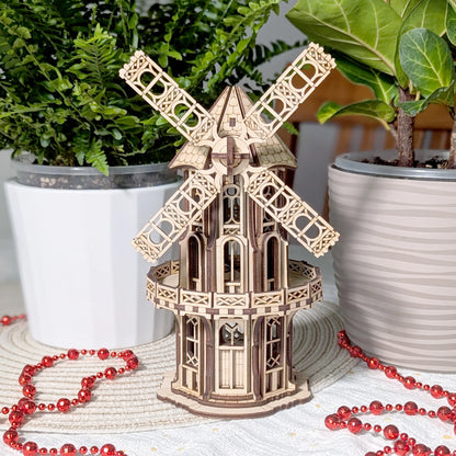 Assembled laser cut plywood Victorian windmill model on a table between potted plants with a festive red beaded garland.