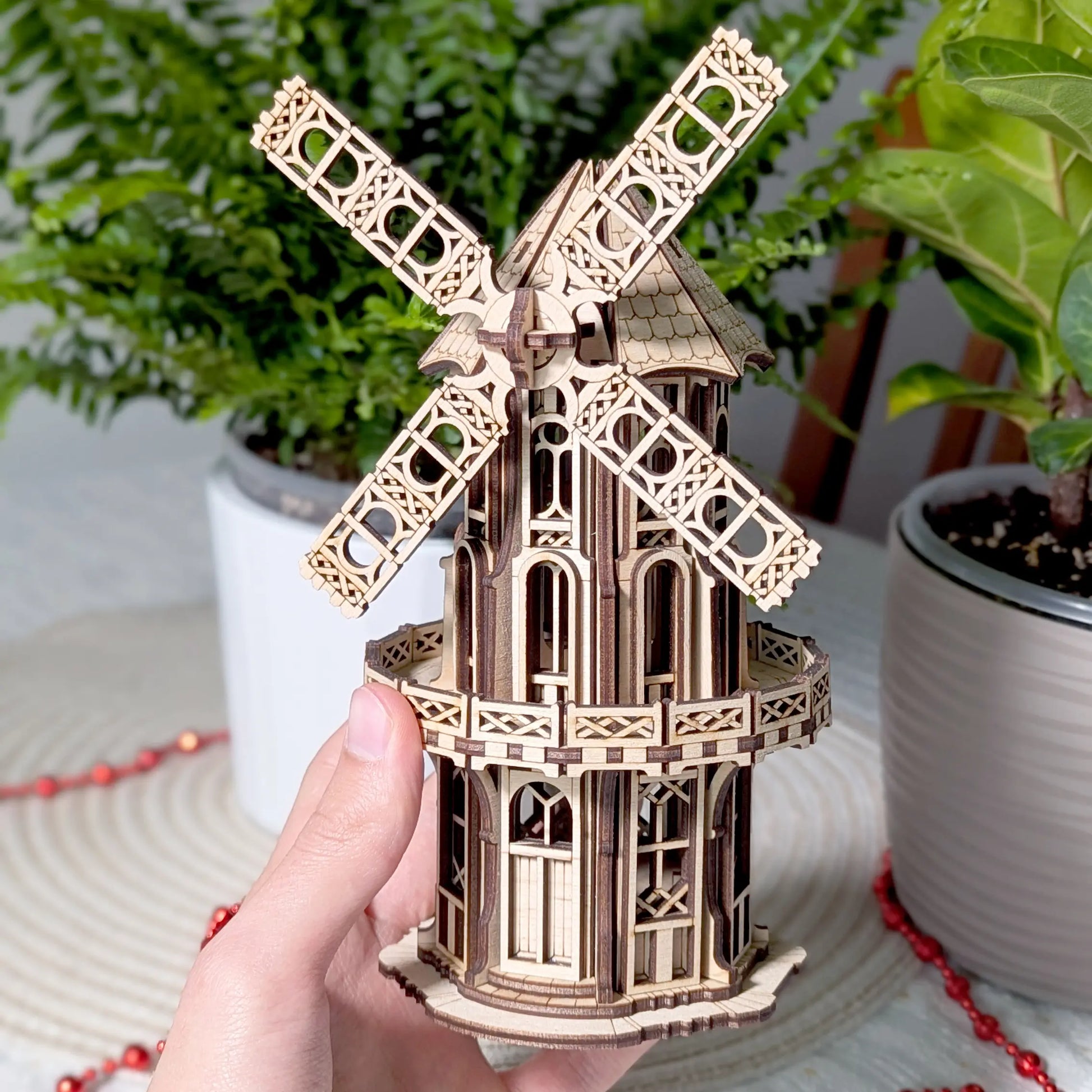 A hand holding up the completed laser cut plywood Victorian windmill model to clearly demonstrate its intricate mini scale.