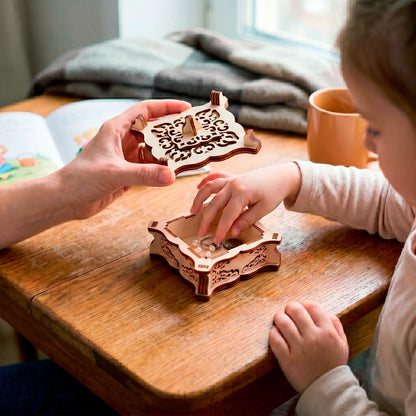 Laser cut plywood vintage trinket box on a wooden desk as adult hands open the carved lid for a small child playing.