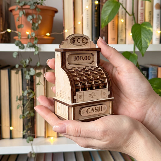 Hands holding a miniature vintage cash register made of laser cut plywood, showing its compact design