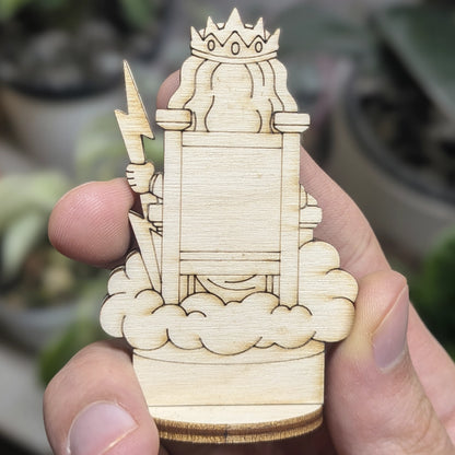 Back view of laser cut plywood Zeus held in hand. Shows dark burnt edges, flowing cape, and natural wood grain texture.