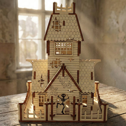 Front view of a laser cut plywood abandoned house featuring a playful skeleton figure in the doorway. The model includes etched vine details on the walls, a crumbling roof aesthetic, and a tall tower, perfect for Halloween decor.