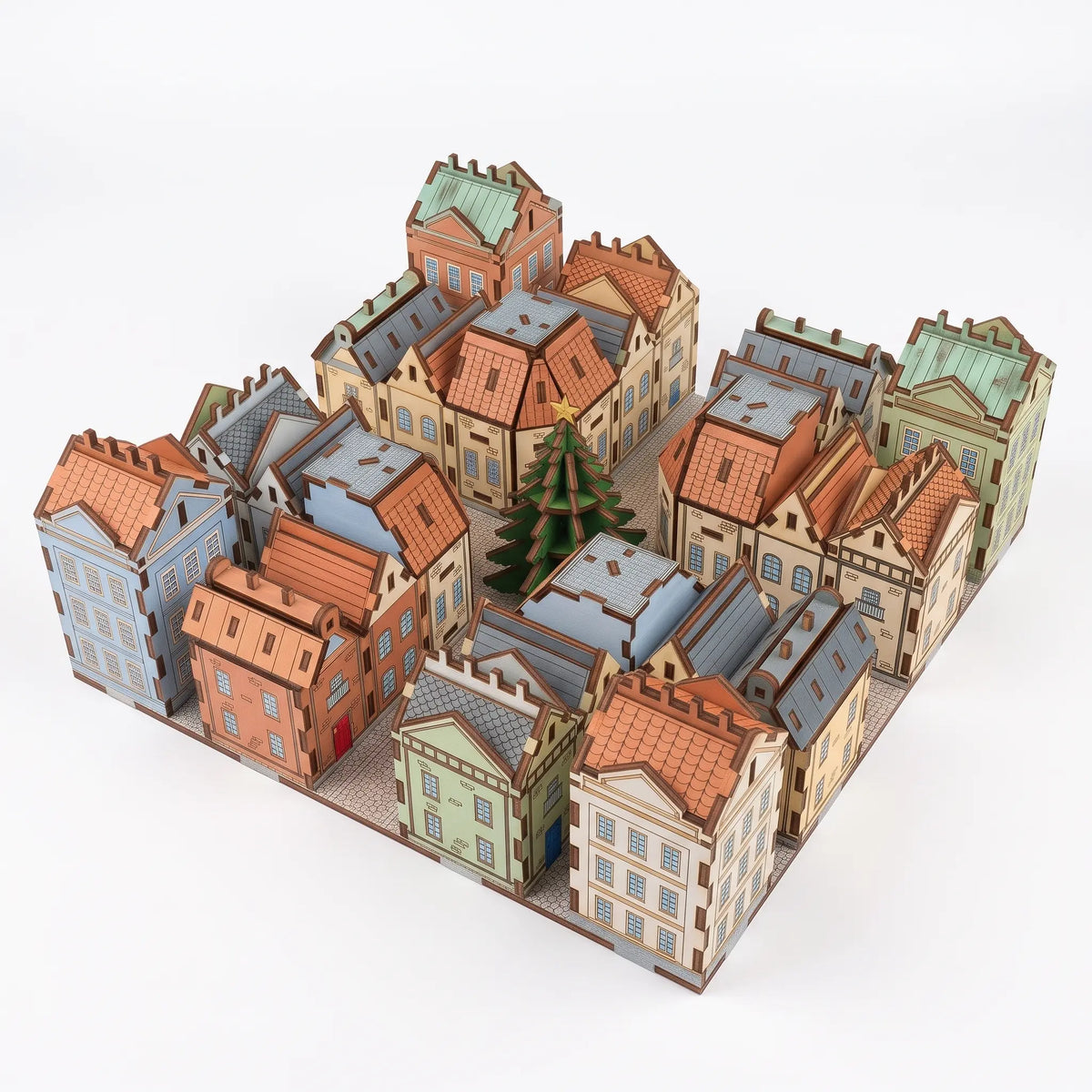 Isometric view of painted laser cut plywood advent calendar village with colorful facades, tiled roofs, and green tree.