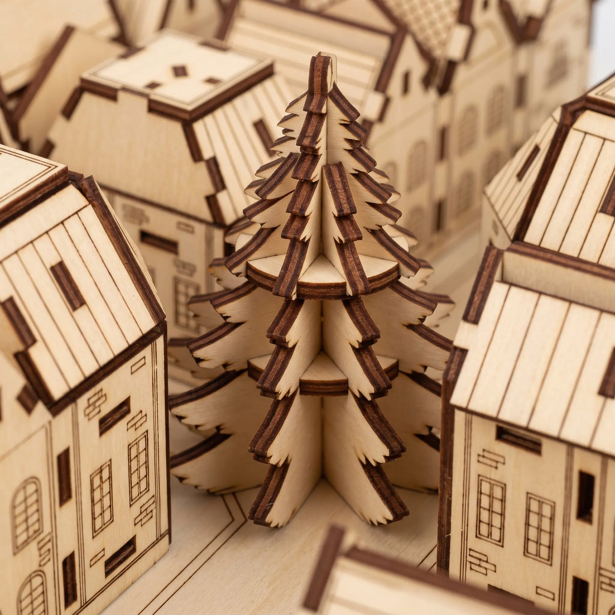 Close-up of laser cut plywood 3D Christmas tree figurine placed between miniature detailed townhouses of advent calendar.