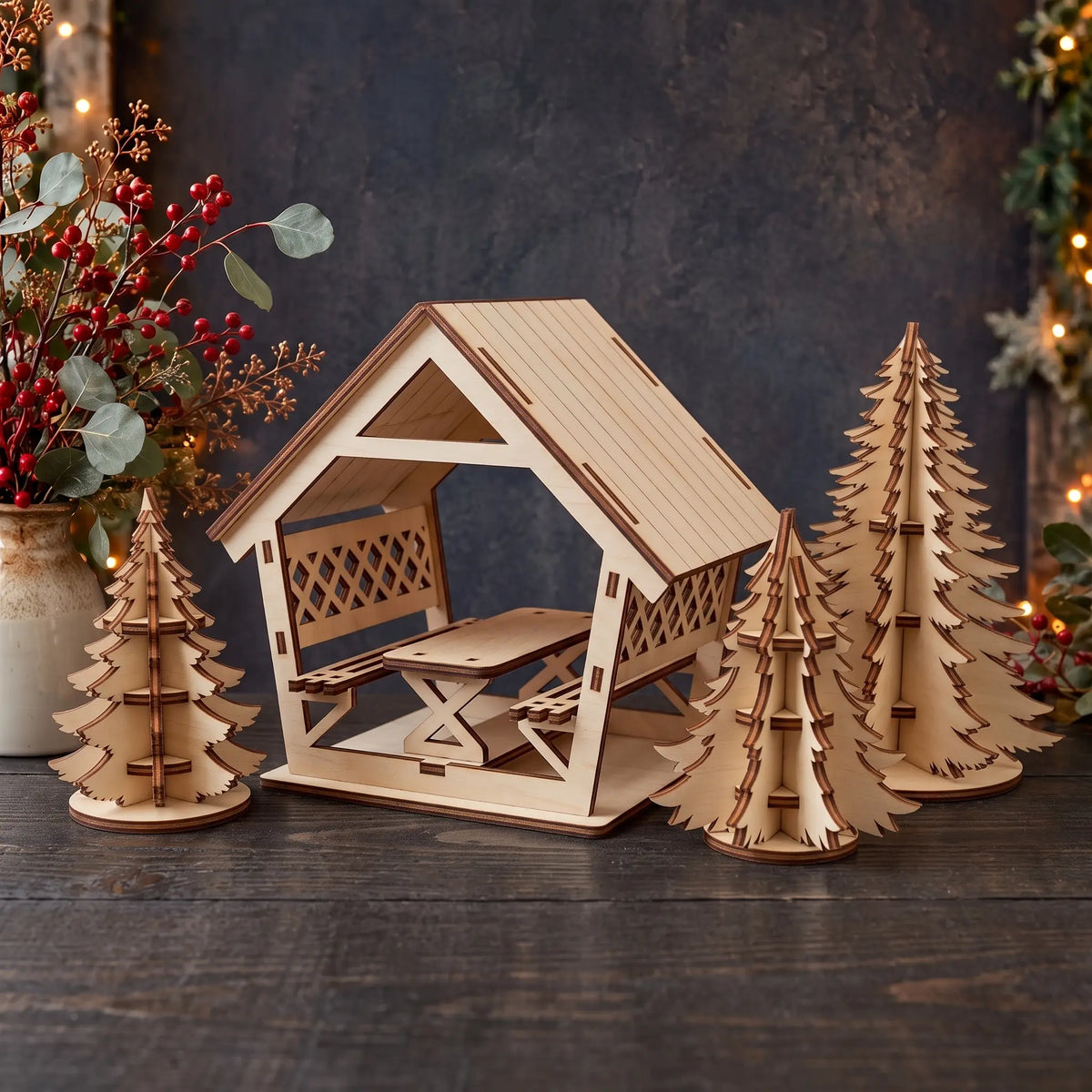 Laser cut plywood miniature gazebo model with picnic table surrounded by slotted pine trees on dark rustic wooden table.