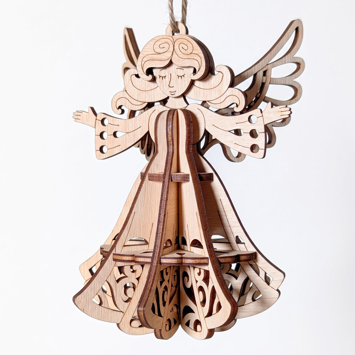 3D laser cut plywood angel ornament with open arms, delicate wings, and tiered filigree skirt hanging on white background.